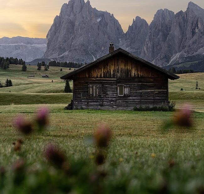 lonely building on meadow behind mounts under sky at sundown